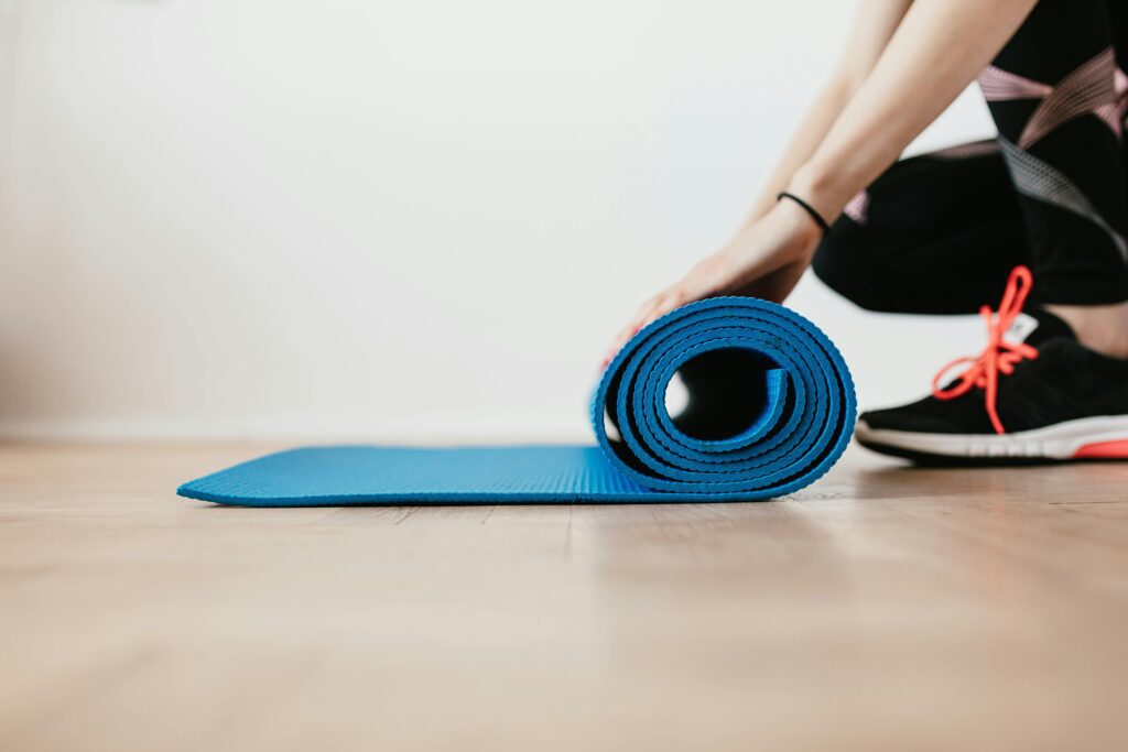 Close-up of a woman preparing for an indoor workout by rolling a blue Pilates mat.